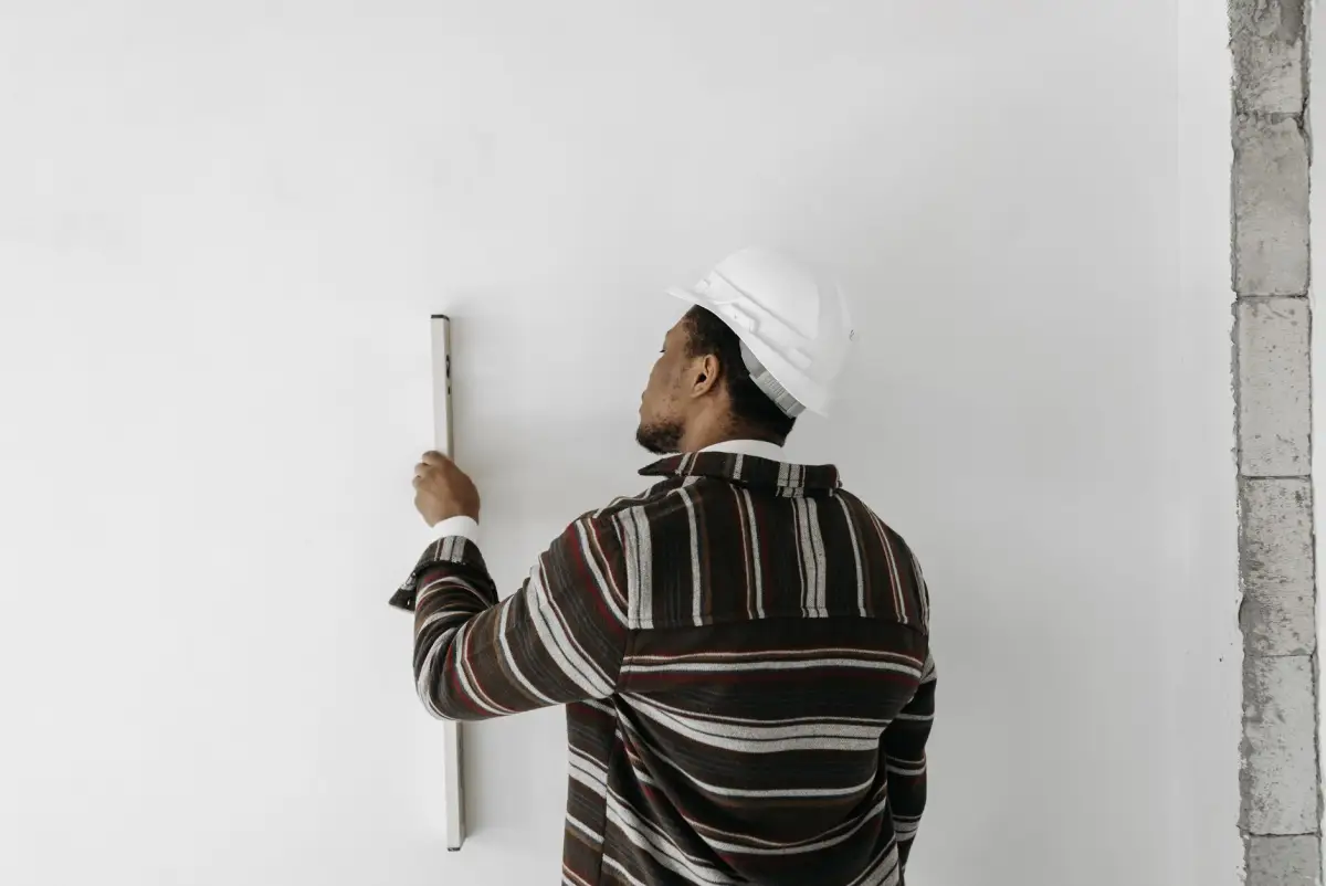 Contractor in a hard hat holding a spirit level against a finished interior wall to check it for plumb